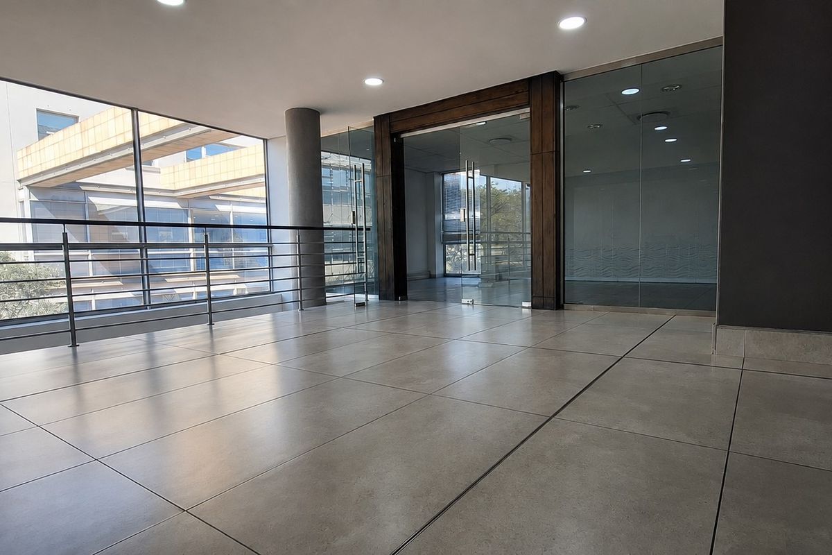 Modern office hallway featuring large format floor tiles, glass partitions, and a stainless steel balustrade, offering a bright and professional open-plan aesthetic.