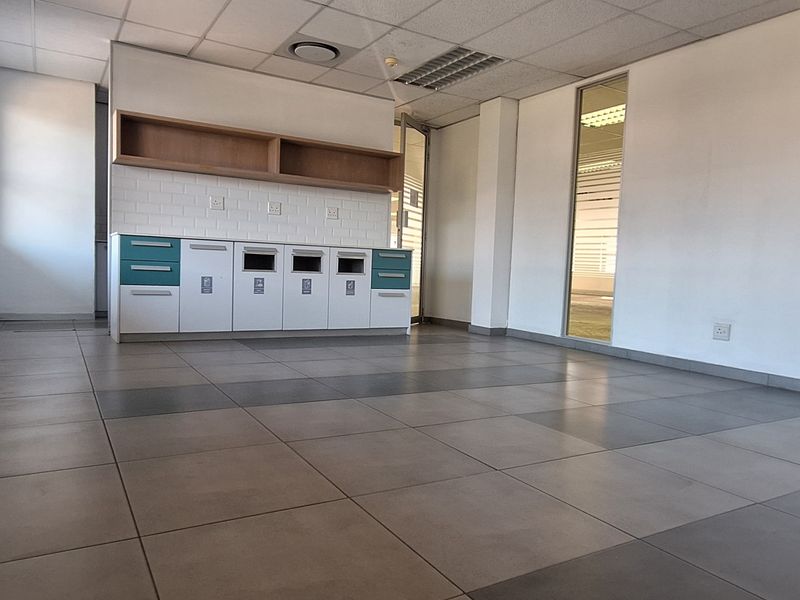 A bright, open-plan office space featuring tiled flooring, a built-in kitchenette area with cabinetry, and modern glass partitions.