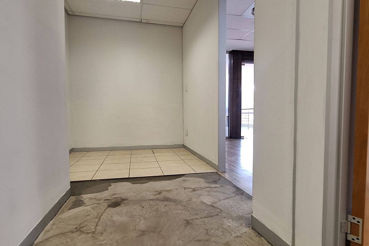 An empty office space featuring a mix of tiled and concrete flooring with a suspended ceiling, ready for custom fit-out.