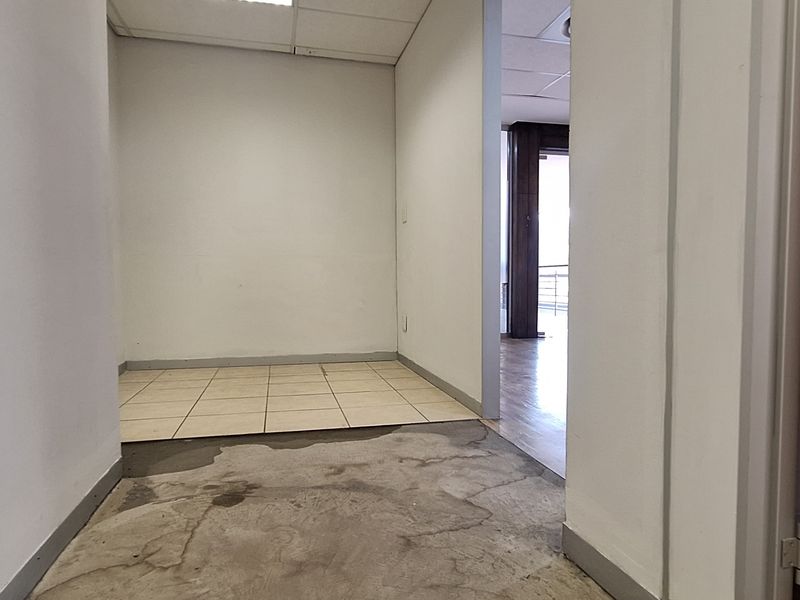 An empty office space featuring a mix of tiled and concrete flooring with a suspended ceiling, ready for custom fit-out.