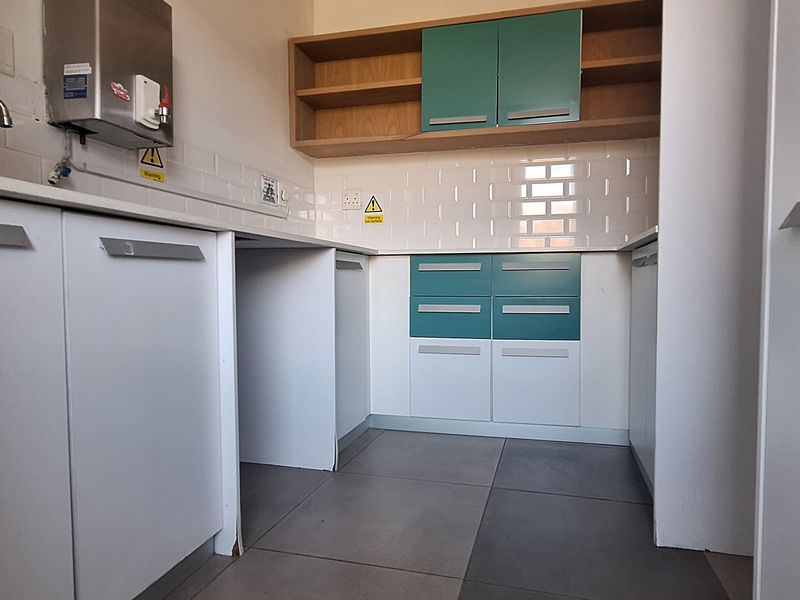 A clean, modern office kitchenette featuring built-in cabinetry, a subway tile backsplash, stone countertops, and a wall-mounted water dispenser.