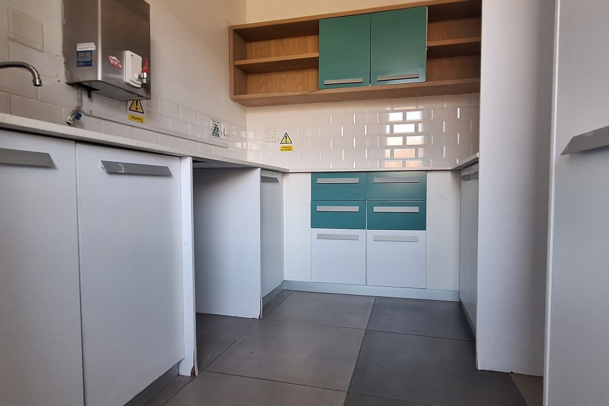 A clean, modern office kitchenette featuring built-in cabinetry, a subway tile backsplash, stone countertops, and a wall-mounted water dispenser.
