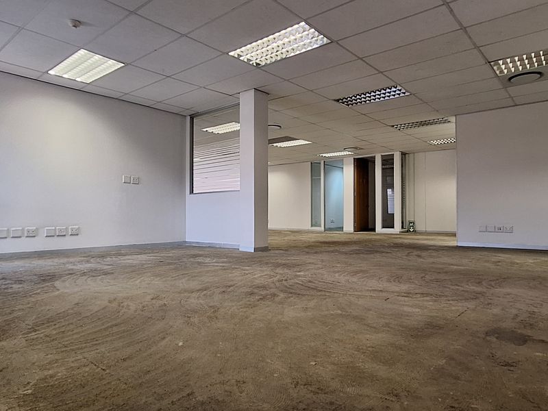 An expansive, vacant open-plan office space featuring a suspended ceiling, recessed lighting, and glass partitioning, currently requiring new flooring installation.