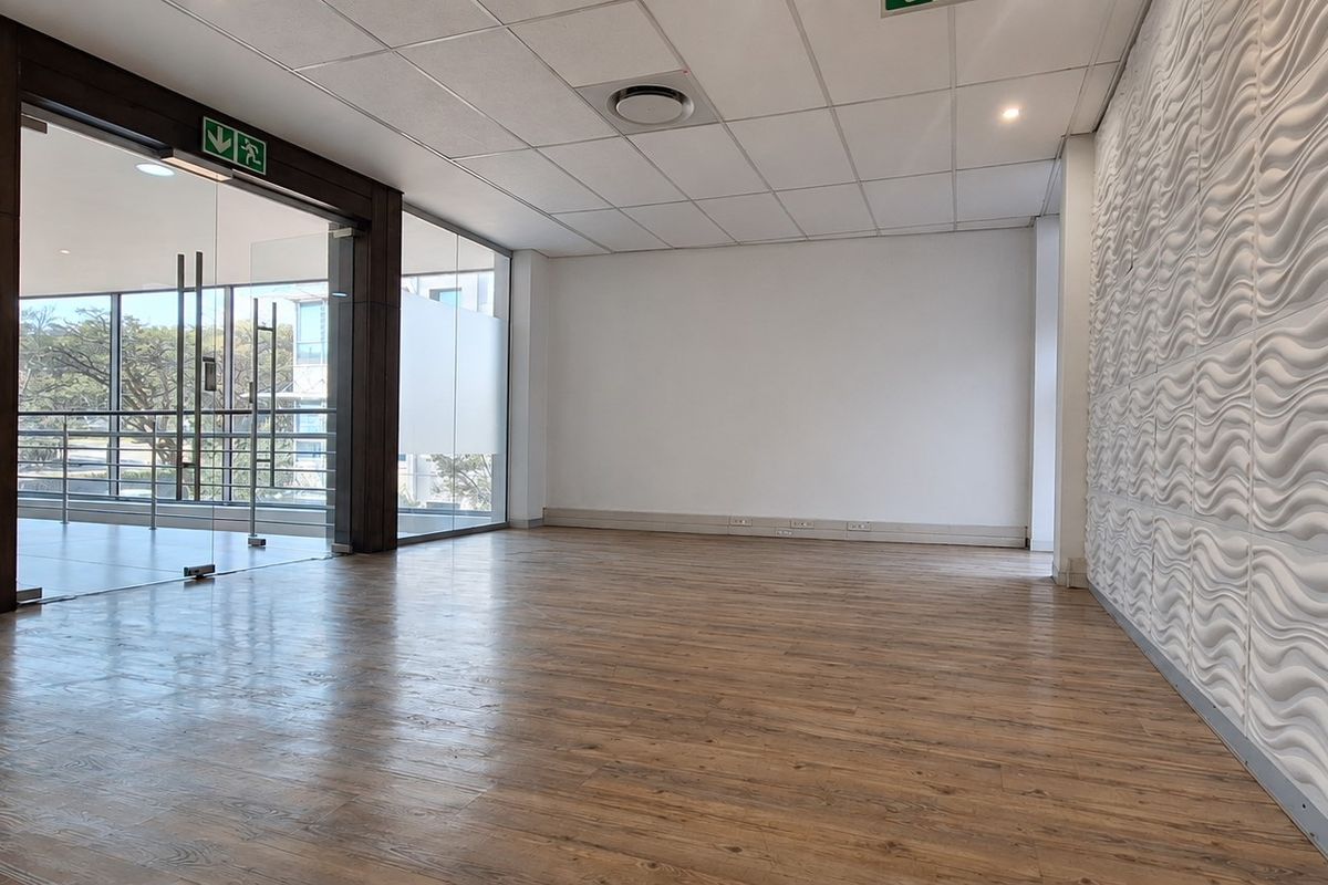 A bright, open-plan office space featuring modern laminate flooring, a textured feature wall, and large glass partitions providing natural light.
