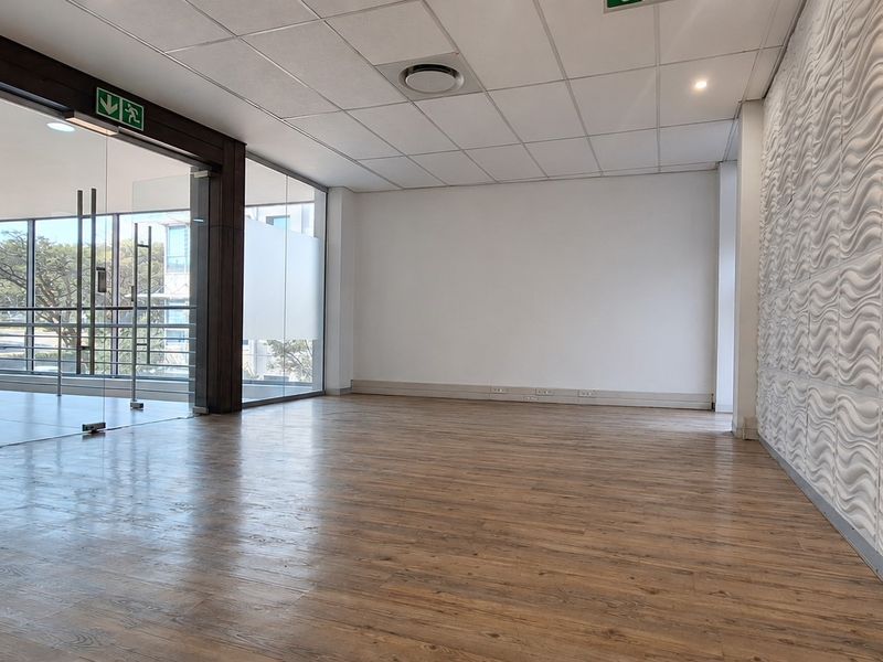 A bright, open-plan office space featuring modern laminate flooring, a textured feature wall, and large glass partitions providing natural light.