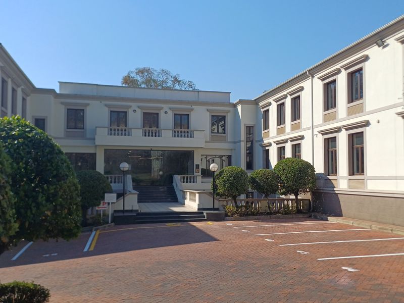 A well-maintained office building exterior featuring a paved parking area, structured facade, and manicured landscaping at the entrance.