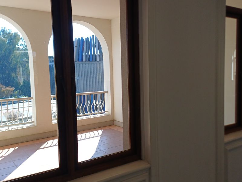 A view from an interior office space looking out onto a covered balcony featuring arched architectural details, tiled flooring, and a metal balustrade.