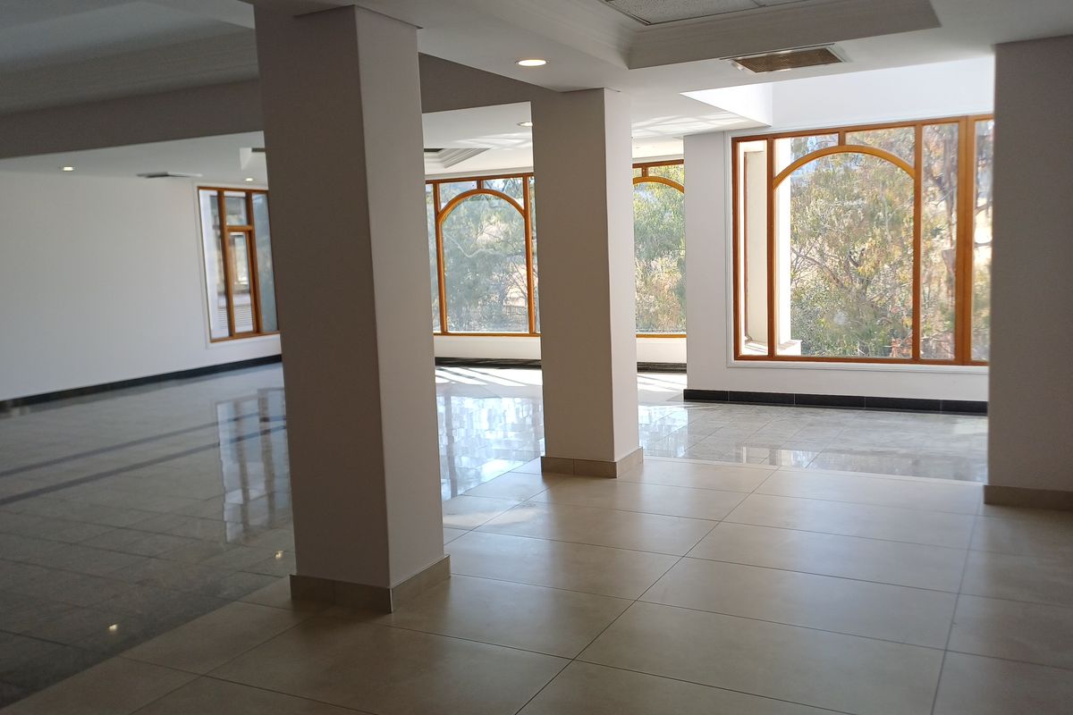 A spacious, empty office area featuring large arched windows, polished tiled flooring, and recessed lighting, offering a bright and professional workspace.