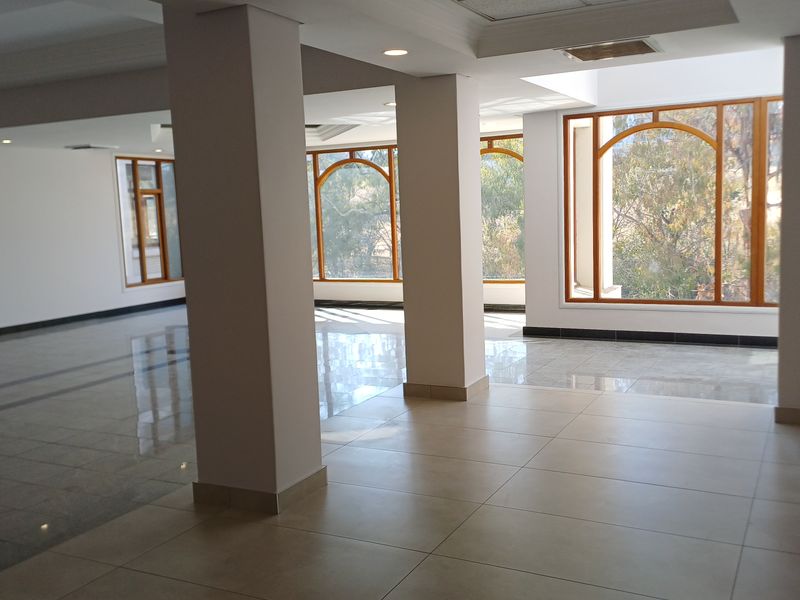 A spacious, empty office area featuring large arched windows, polished tiled flooring, and recessed lighting, offering a bright and professional workspace.