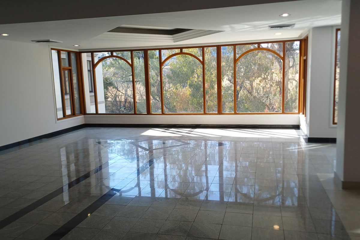 Spacious, empty office area featuring polished granite flooring, large arched windows with natural light, and recessed ceiling lighting.
