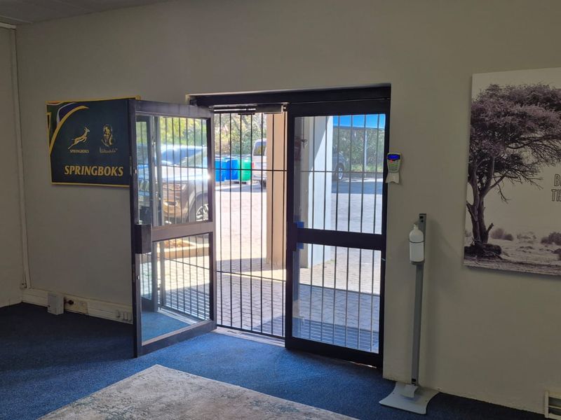 An industrial entry area featuring a secure glass door with an integrated security gate and blue carpet flooring.