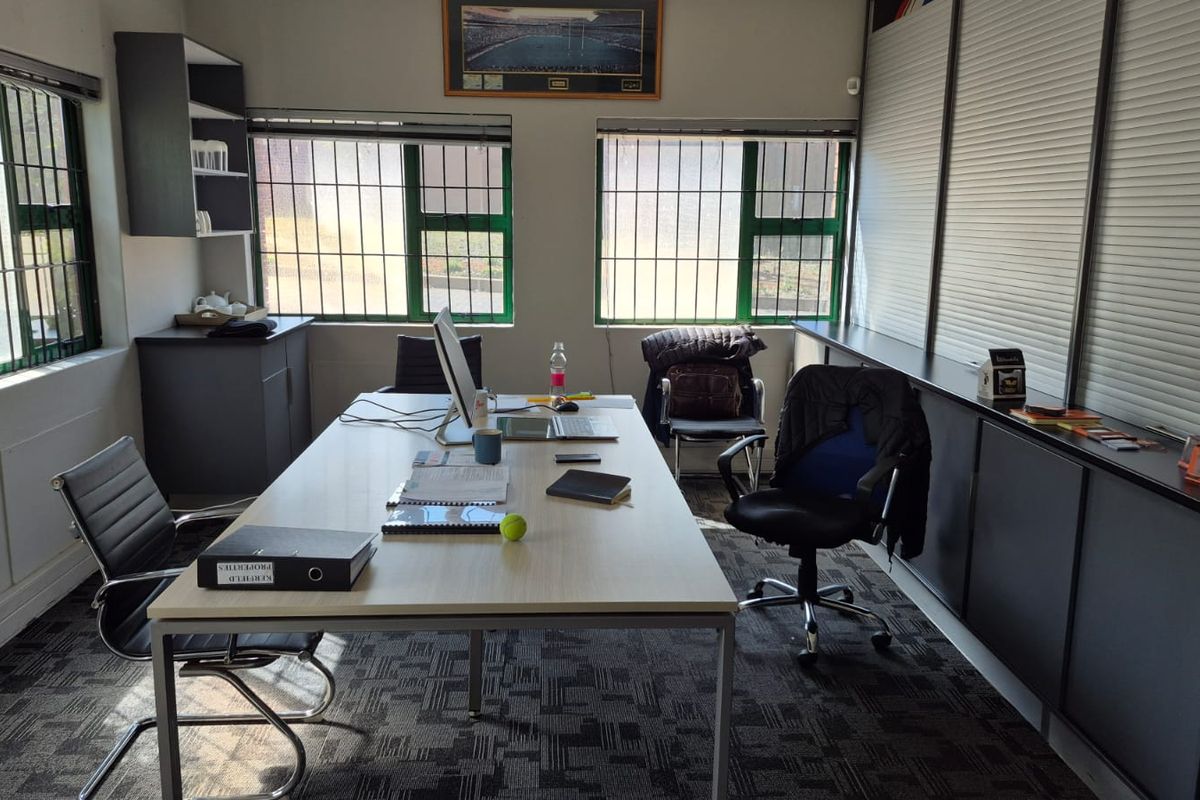 A functional office space featuring built-in cabinetry, security bars on windows, and carpeted flooring, suitable for professional use.