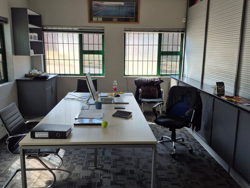 A functional office space featuring built-in cabinetry, security bars on windows, and carpeted flooring, suitable for professional use.