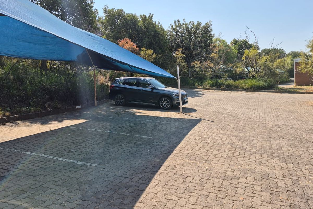 An outdoor paved parking area featuring a blue shade cloth structure for vehicle protection.