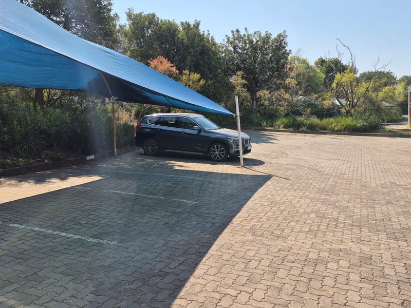 An outdoor paved parking area featuring a blue shade cloth structure for vehicle protection.