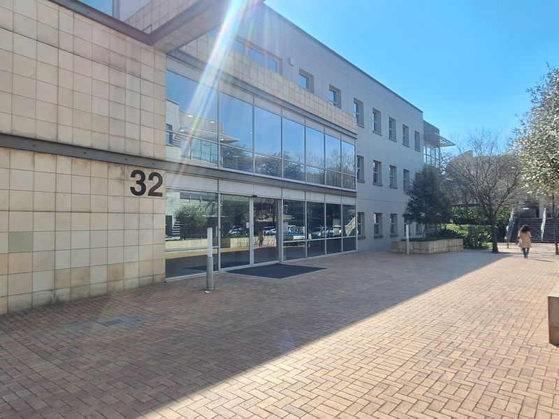 Front exterior view of a modern office building featuring stone cladding, extensive glass curtain walling, and a paved entrance area.