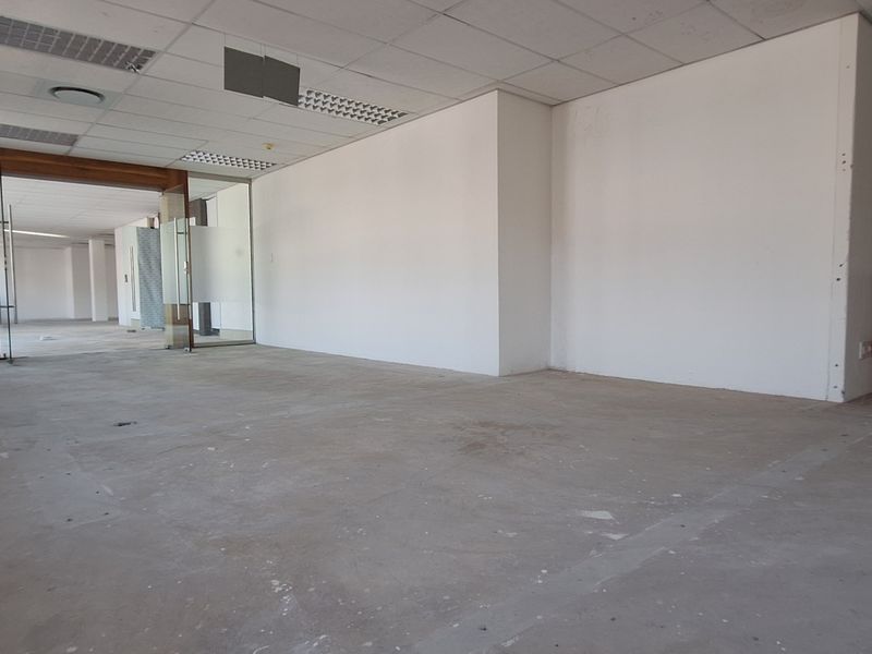 An open-plan office space featuring a suspended ceiling, glass partitioning, and a small kitchenette area, currently in a vacant, unfinished state.