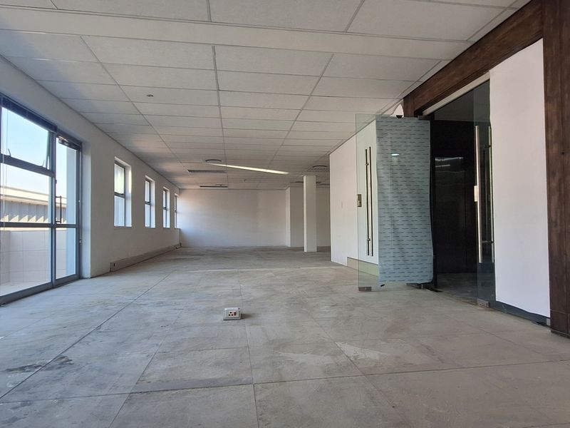 A spacious, empty open-plan office area featuring large windows, suspended ceilings, and glass partition doors, offering a blank canvas for professional workspace customization.