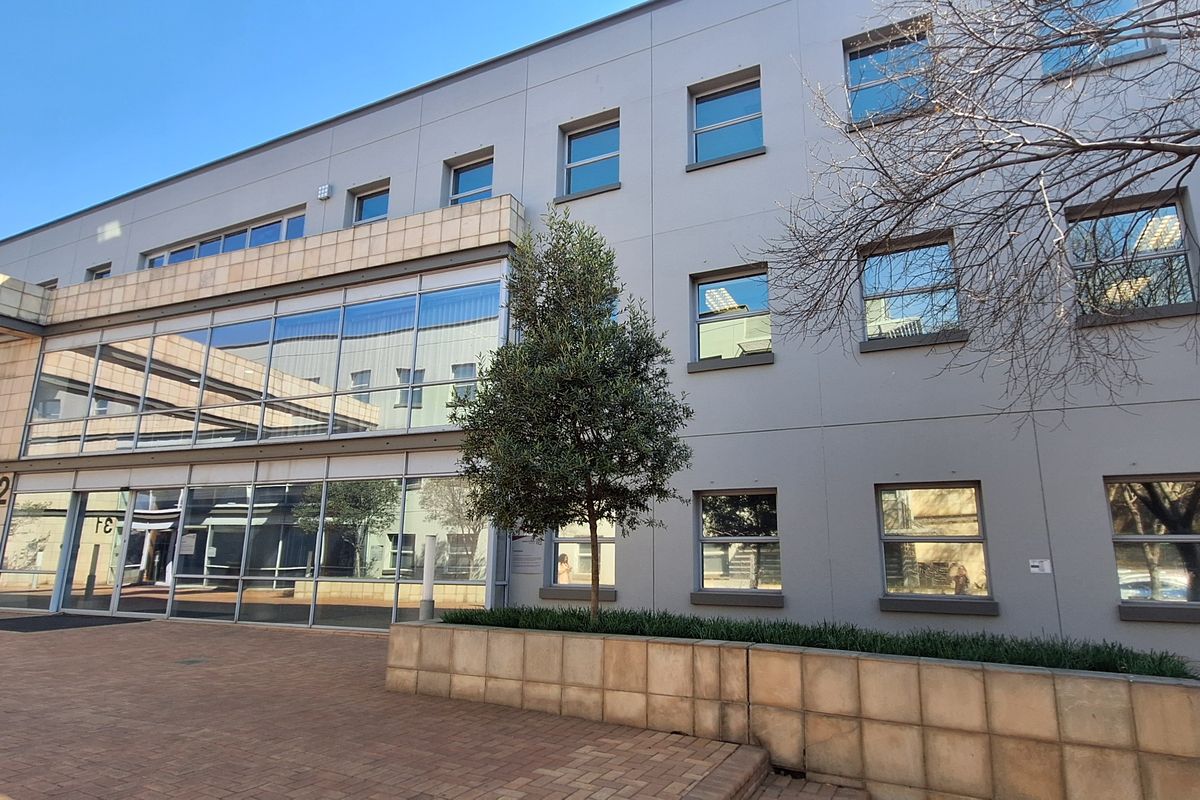 Modern office building exterior featuring a glass facade, stone cladding, and a paved entrance area with integrated landscaping.