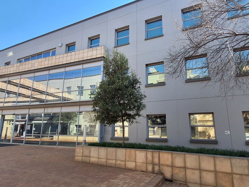 Modern office building exterior featuring a glass facade, stone cladding, and a paved entrance area with integrated landscaping.