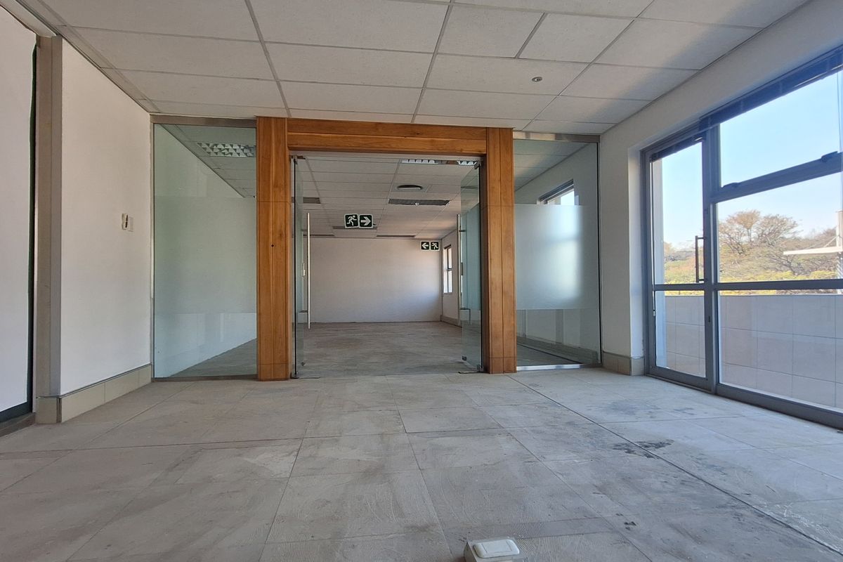 An open-plan office space featuring glass partitions, timber framing, large windows providing natural light, and a suspended ceiling.