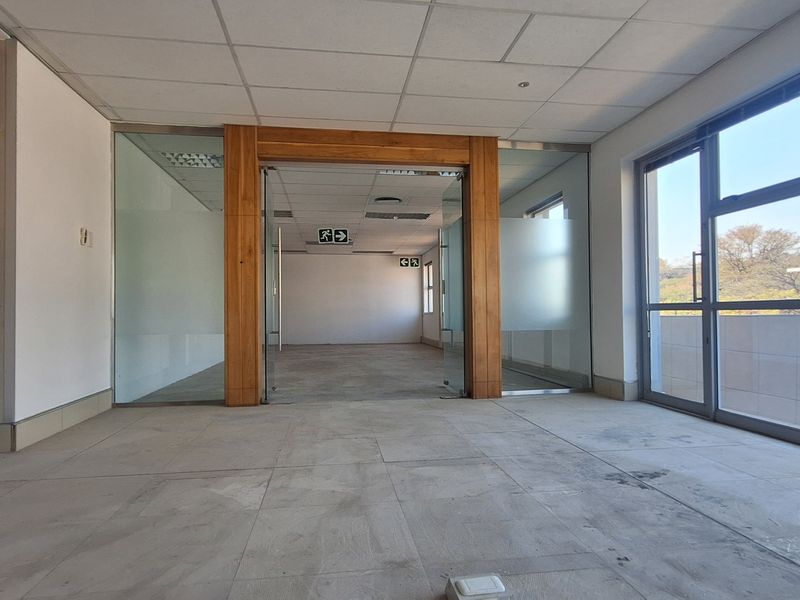 An open-plan office space featuring glass partitions, timber framing, large windows providing natural light, and a suspended ceiling.