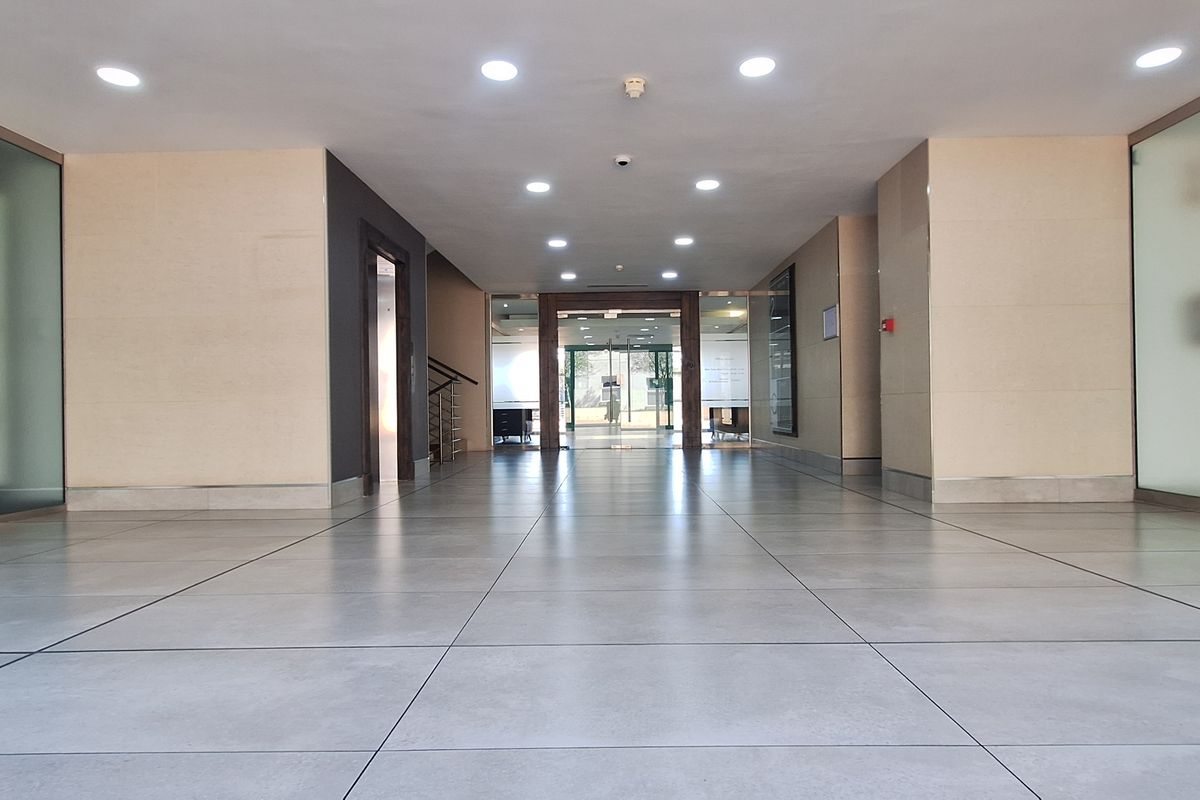 A spacious and modern office building entrance lobby featuring tiled flooring, recessed lighting, and frosted glass partitions leading to internal office spaces.
