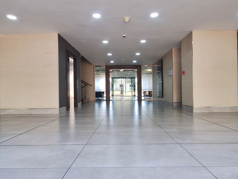 A spacious and modern office building entrance lobby featuring tiled flooring, recessed lighting, and frosted glass partitions leading to internal office spaces.