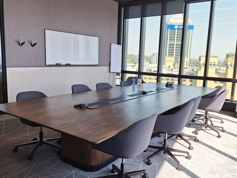 Modern professional boardroom featuring a large integrated meeting table, floor-to-ceiling windows with city views, and high-quality finishes.