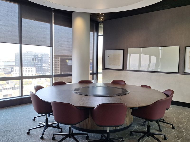 A modern circular boardroom featuring floor-to-ceiling windows with city views, a recessed ceiling detail, and high-quality finishes.