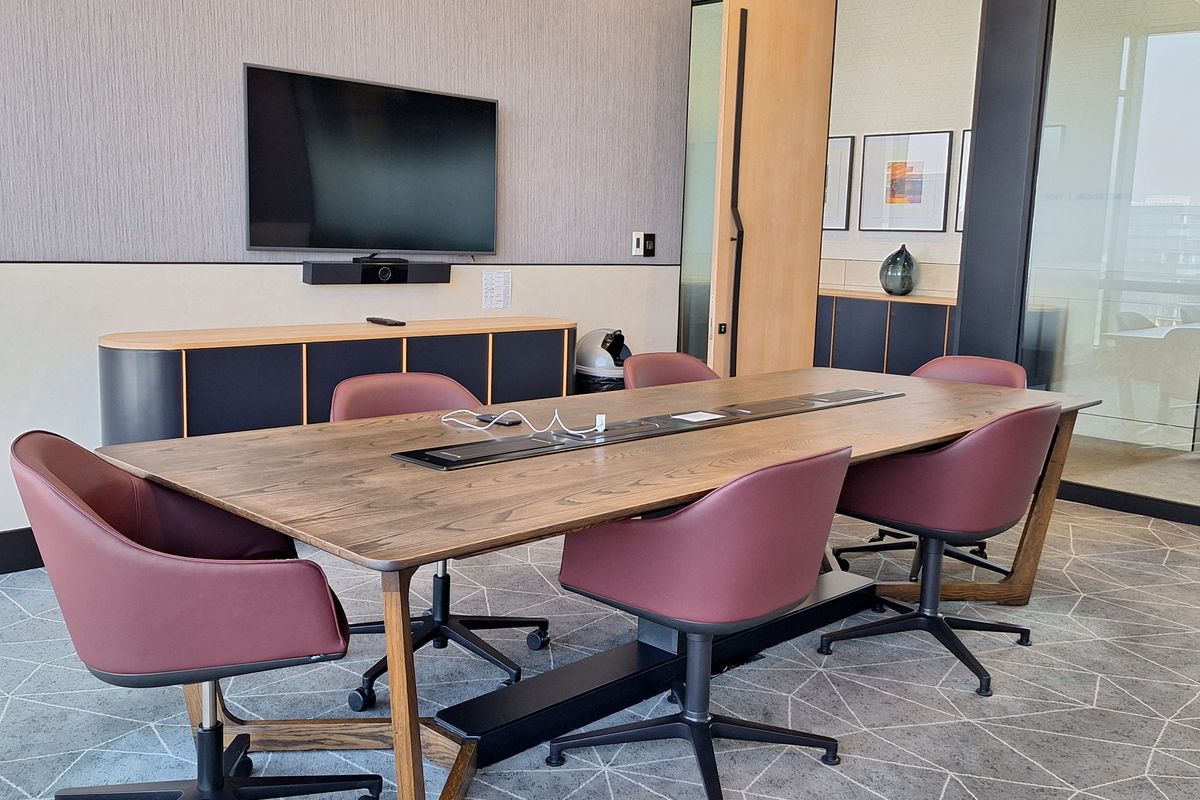 Modern professional boardroom featuring a large wooden conference table with integrated power, glass partition walls, and built-in storage cabinetry.