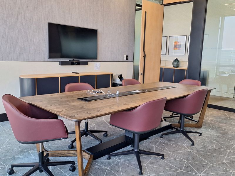 Modern professional boardroom featuring a large wooden conference table with integrated power, glass partition walls, and built-in storage cabinetry.