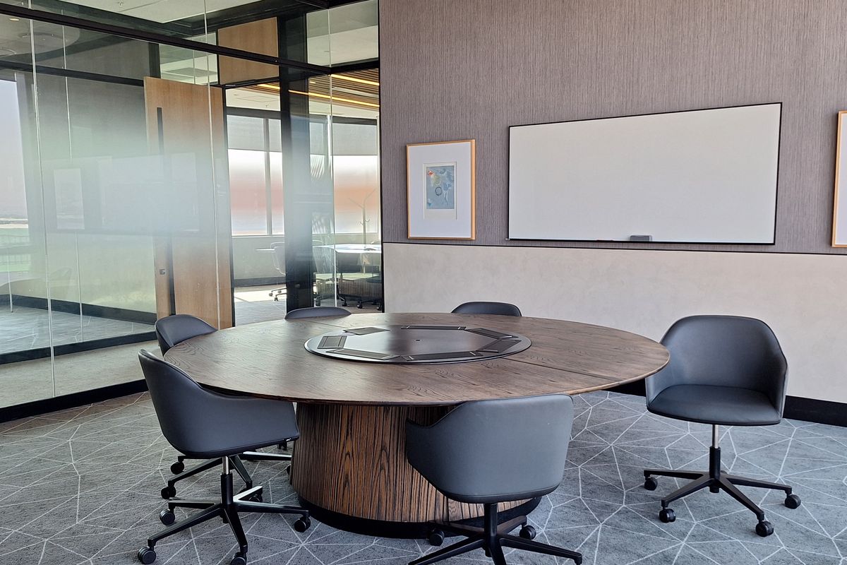 A modern, professional office meeting room featuring glass partitions, a circular conference table, and contemporary carpet flooring.