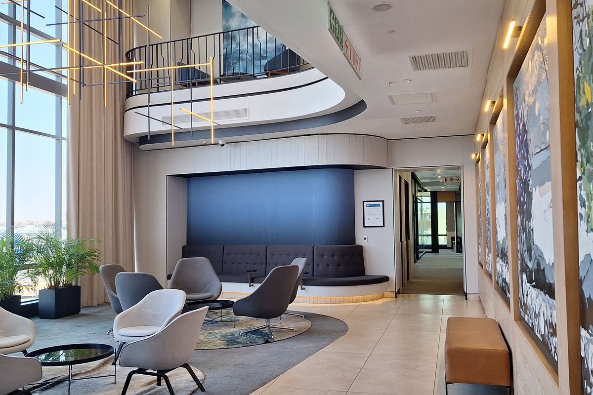 Modern office lobby featuring double-volume ceilings, floor-to-ceiling windows, a mezzanine level, and high-quality finishes throughout.