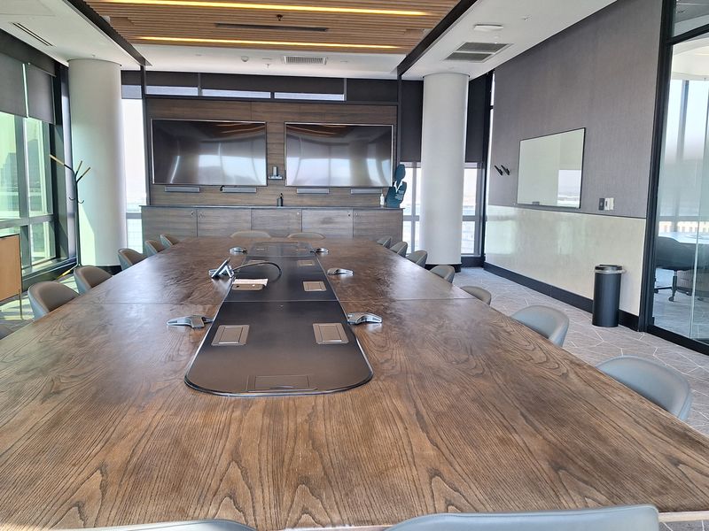 Modern professional boardroom featuring a large timber conference table, slatted wood ceiling, integrated media screens, and glass partition walls for a sleek corporate aesthetic.