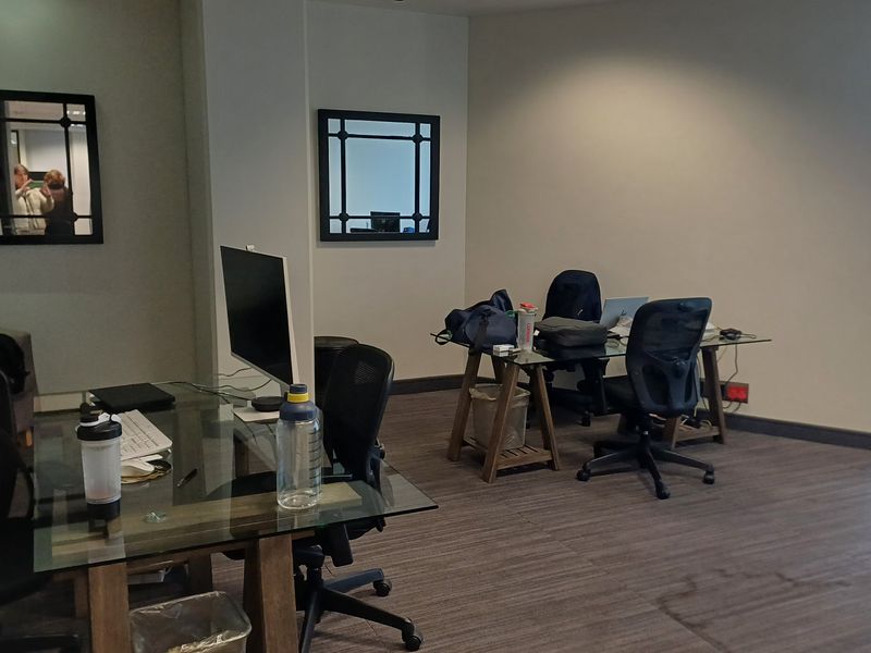 A functional office space featuring large windows for natural light, neutral wall finishes, and carpeted flooring, suitable for a professional work environment.
