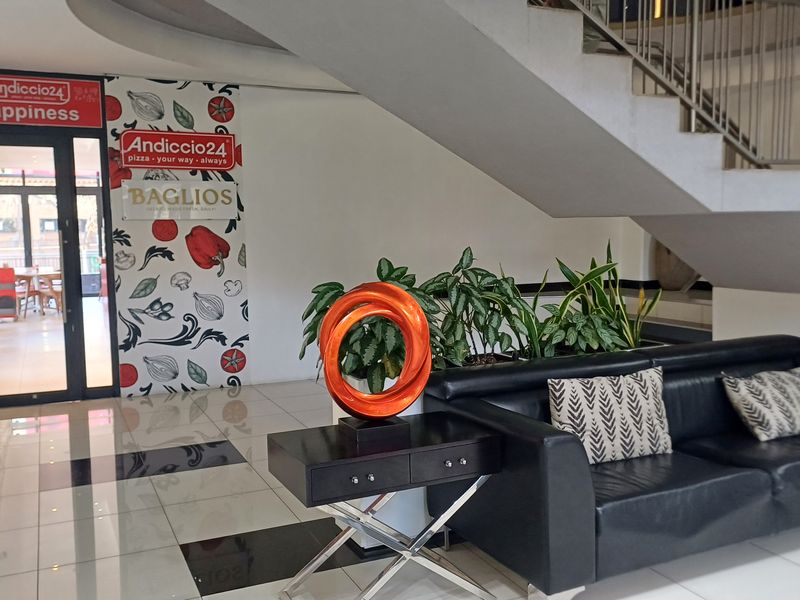 A bright office building entrance lobby featuring polished tiled flooring, a modern staircase with metal balustrades, and clear access to commercial units.