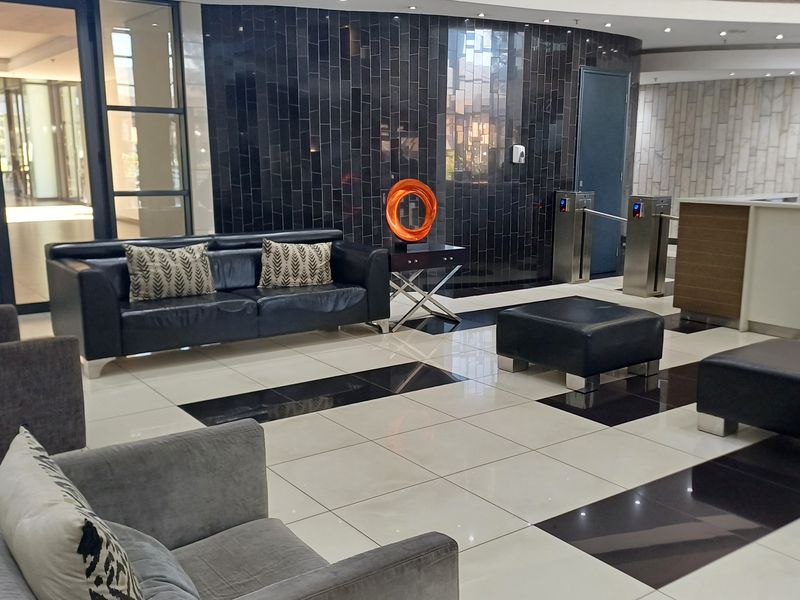 Modern office building lobby featuring a reception area, security turnstiles, high-gloss tiled flooring, and a decorative dark tiled feature wall.