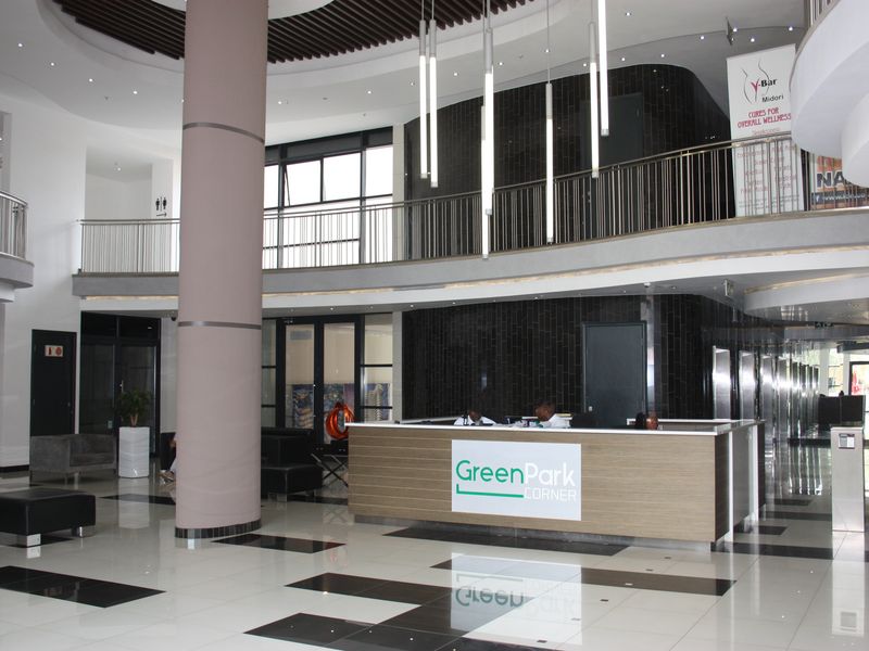 Spacious modern office building lobby featuring a central reception desk, mezzanine level with metal railings, and polished tiled flooring.