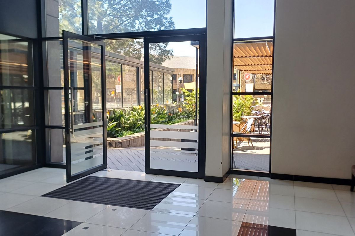 Bright and modern office entrance featuring large glass doors, floor-to-ceiling windows, and polished tiled flooring, providing seamless access to an outdoor patio area.