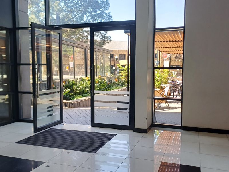 Bright and modern office entrance featuring large glass doors, floor-to-ceiling windows, and polished tiled flooring, providing seamless access to an outdoor patio area.