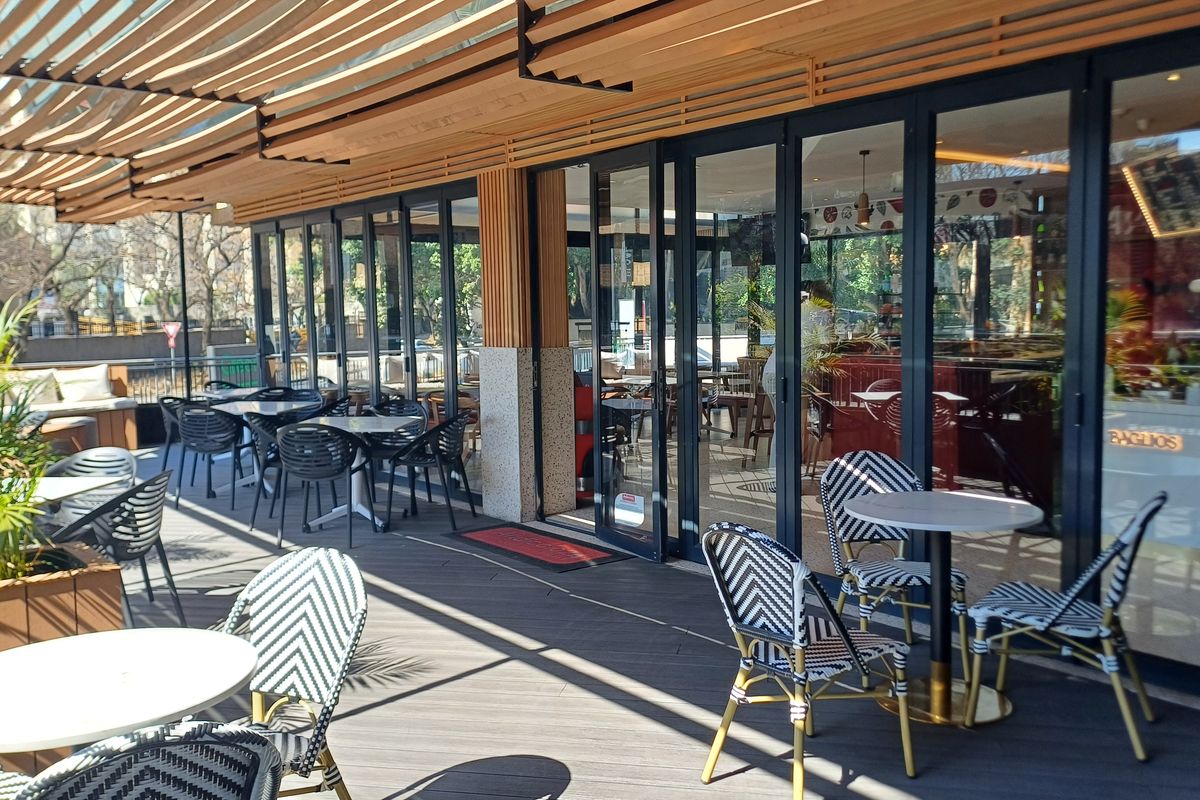 A modern outdoor patio area featuring composite decking, a timber slat pergola, and full-height glass folding doors providing seamless access to the office interior.