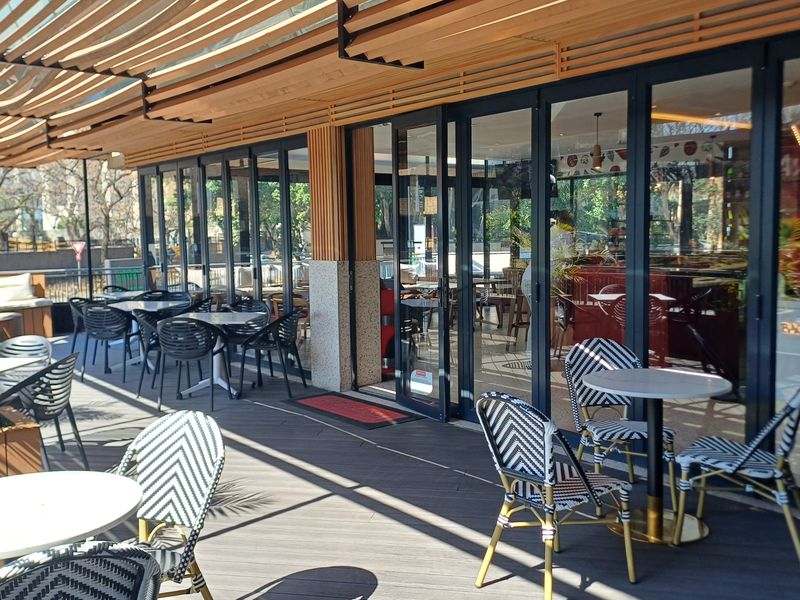 A modern outdoor patio area featuring composite decking, a timber slat pergola, and full-height glass folding doors providing seamless access to the office interior.