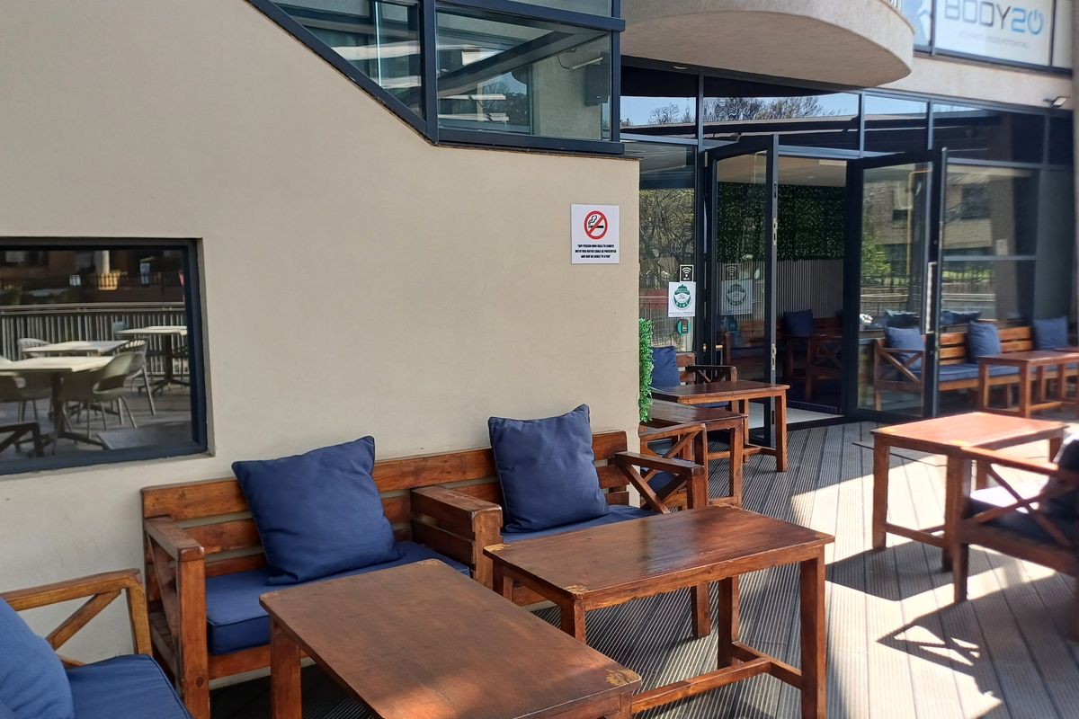 A covered outdoor patio area featuring timber decking and large glass sliding doors providing access to the office interior.
