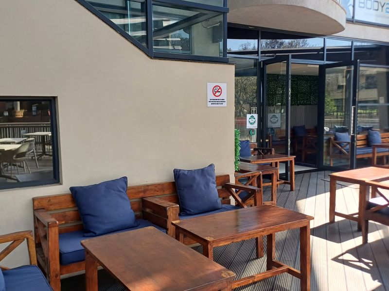 A covered outdoor patio area featuring timber decking and large glass sliding doors providing access to the office interior.