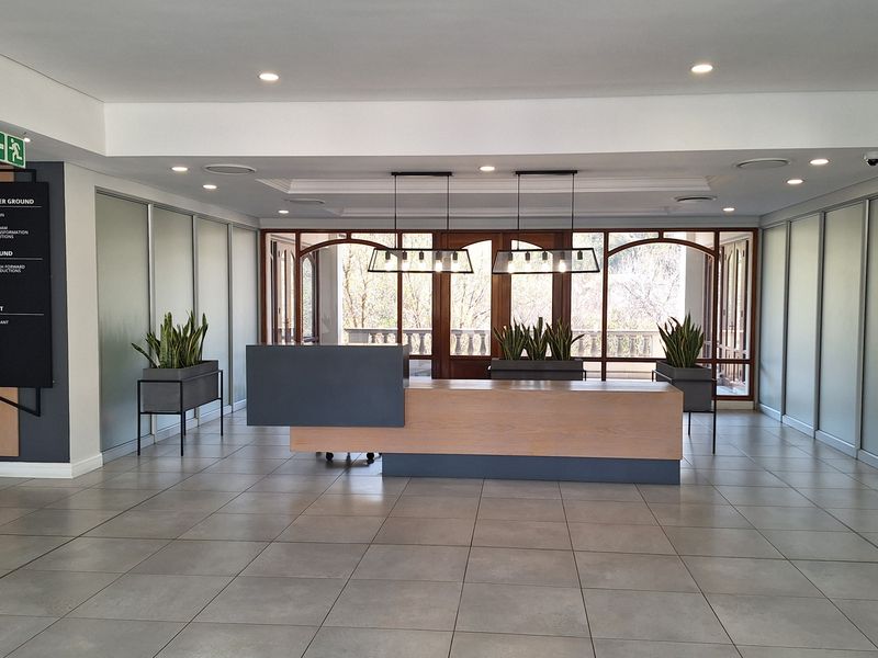 Modern office reception area featuring a contemporary reception desk, large format floor tiles, recessed lighting, and glass-paneled entrance doors.