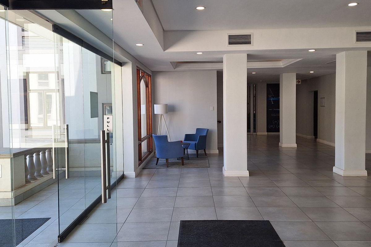A bright and spacious office building entrance lobby featuring large glass doors, tiled flooring, and structural columns.