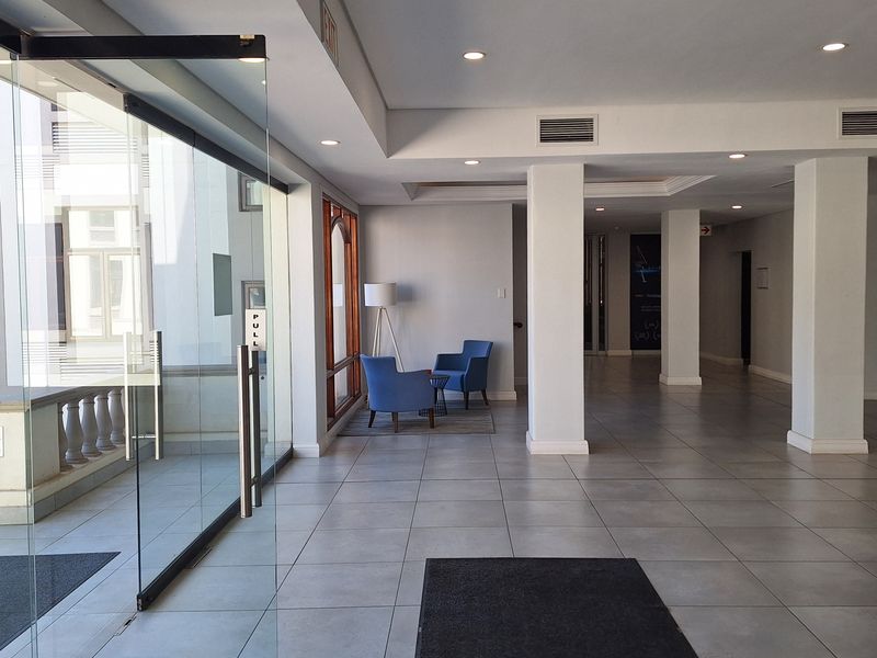 A bright and spacious office building entrance lobby featuring large glass doors, tiled flooring, and structural columns.