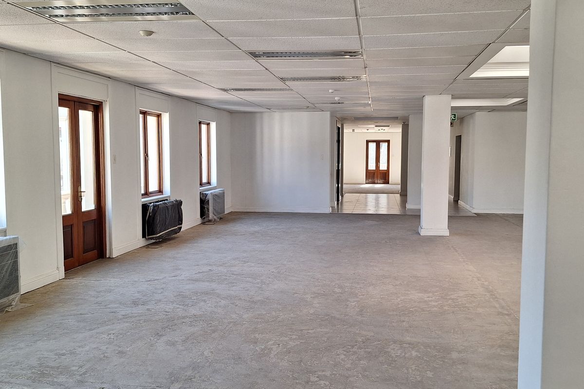 A spacious, vacant open-plan office area featuring a suspended ceiling, recessed lighting, and large wooden-framed doors, ready for custom fit-out.