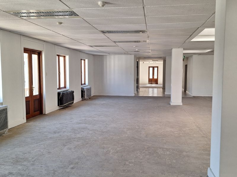 A spacious, vacant open-plan office area featuring a suspended ceiling, recessed lighting, and large wooden-framed doors, ready for custom fit-out.